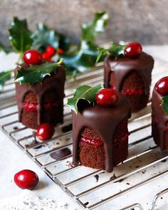 small cakes with chocolate frosting and cherries on a cooling rack next to holly