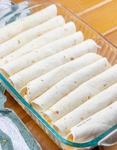 a glass baking dish filled with tortillas on top of a wooden table next to a towel