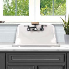 a white kitchen sink sitting under a window next to a potted plant and green plants