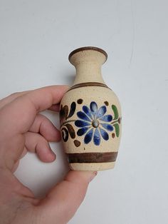 a hand holding a small ceramic vase with blue flowers on the outside and brown trim