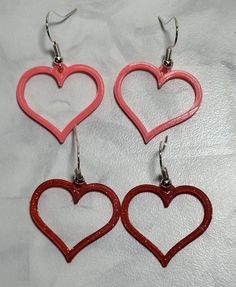 three red heart shaped earrings on a white surface with silver earwires and hooks