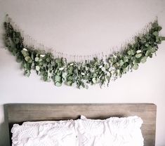 a bed with white sheets and green plants on the headboard, hanging above it