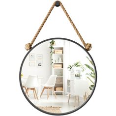 a mirror hanging from a rope in front of a white table with chairs and plants