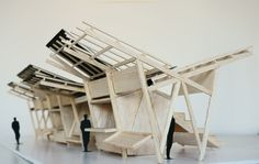 two people are standing in front of a sculpture made out of chairs and ladders