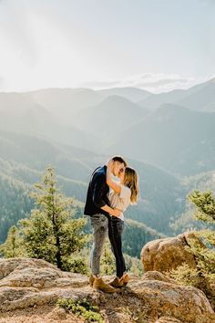 a man and woman kissing on top of a rock in front of the mountain range