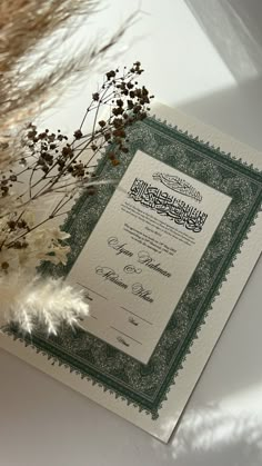 the certificate is next to some dried flowers and feathers on a white tablecloth with green trimmings