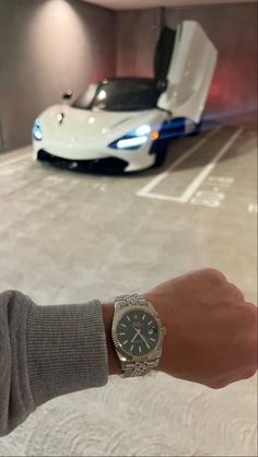 a person holding onto a wrist watch in front of a white sports car with its door open