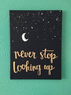 a black and gold sign that says never stop looking up with the moon in the background