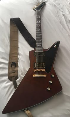 an electric guitar laying on top of a bed next to a case with a strap