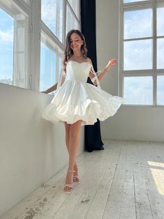 a woman standing in front of a window wearing a white dress