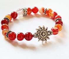 SUNFIRE Bracelet by Evil Queen Jewelry Natural Banded Agate in Sunset Fire Colors, Red Orange, a yellow and White Antique Silver Sun is the focal with antique Silver Accent Beads. Polished, Smooth, Natural Stone Stretch Bracelet measuring approximately 7 inches with 8mm round stones If you need a different length, please contact me! Each Stone is Unique and made by nature, no two are alike As with all jewelry, wear with care. Stones and metal do not always do well with chemicals or water. Best t Cheap Red Bracelets With Colorful Beads, Red Carnelian Beaded Bracelets, Adjustable Red Agate Crystal Bracelet, Red Agate Gemstone Beaded Bracelets, Red Crystal Bracelet With Natural Stones, Red Natural Stones Crystal Bracelet, Fire Bracelet, Orange Accessories, Silver Shamrock