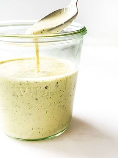 a spoon is pouring dressing into a glass jar