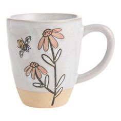 a coffee cup with flowers and bees painted on the side, sitting in front of a white background