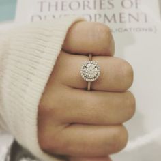 a close up of a person's hand with a ring on their finger and a book in the background