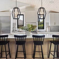 four stools sit in front of an island with three lights hanging from the ceiling