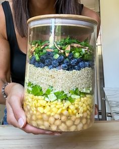 a woman holding up a jar filled with different types of vegetables and grains in it