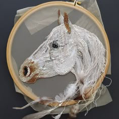 a close up of a horse in a hoop with some feathers on the side and an embroidered piece of fabric behind it