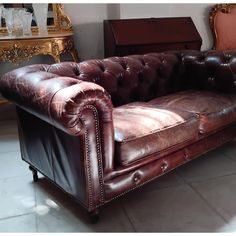 a brown leather couch sitting on top of a tile floor next to a mirror and table