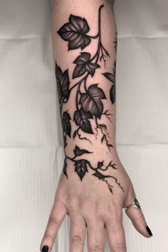 a woman's hand with black flowers and leaves tattoo on it, showing the ring finger