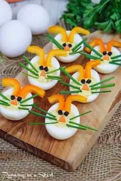 deviled eggs decorated like cats with carrots and green onions on a cutting board