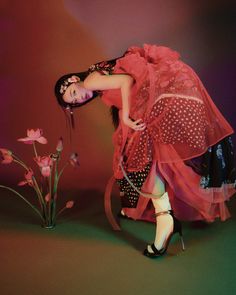 a woman in a red dress and high heeled shoes is leaning on a chair