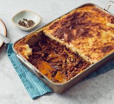 a casserole dish with meat and cheese in it on a blue towel next to two plates