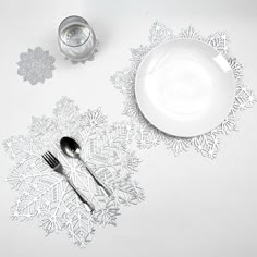 a white table with silverware and snowflakes on the placemats, next to a glass of water