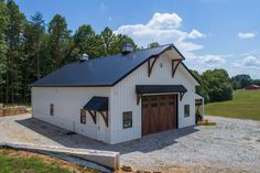 a large white barn with a black roof and two garage doors on the side of it