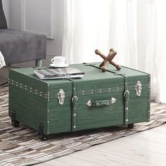 a green trunk sitting on top of a rug in front of a chair and coffee table