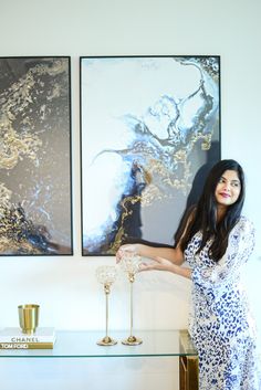 a woman standing next to a glass table in front of two paintings on the wall