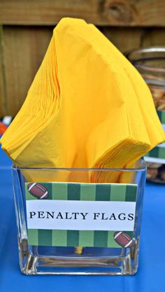 a yellow napkin sits in a clear cup on top of a blue table cloth covered table