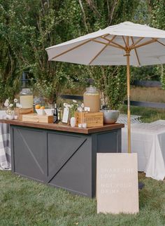 an outdoor bar set up with bottles and jars on it, near a picnic table