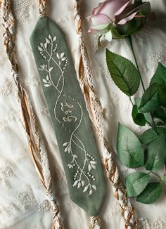 two pieces of cloth with embroidered designs on them next to some green leaves and flowers