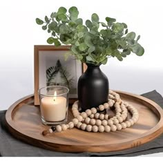 a wooden tray with a vase and beads on it, next to a candle holder