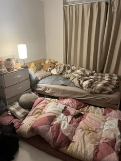 an unmade bed in the corner of a room with stuffed animals and blankets on it