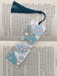 two bookmarks with blue flowers and tassels on top of an open book