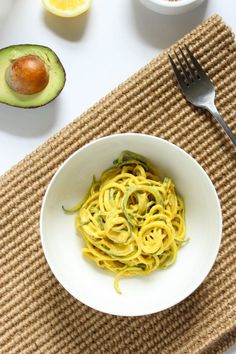 a white bowl filled with noodles next to an avocado