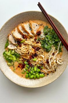 a bowl filled with noodles, meat and veggies next to chopsticks