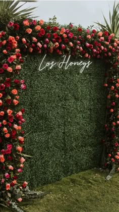 a lush green wall covered in flowers and greenery with the word love among it