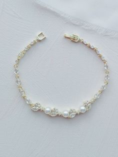 a bracelet with pearls and gold beads on a white cloth covered surface, the bead is attached to an adjustable clasp