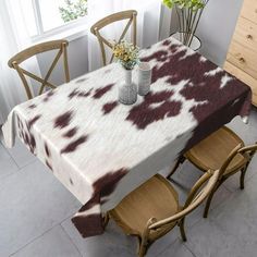 a cow print tablecloth on a dining room table with chairs and flowers in vases