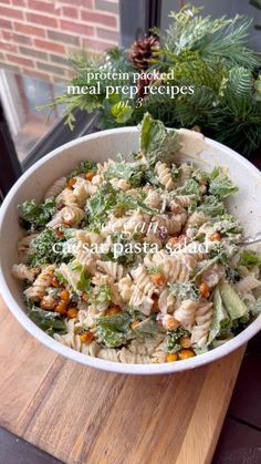 a bowl filled with pasta and vegetables on top of a wooden table next to a potted plant