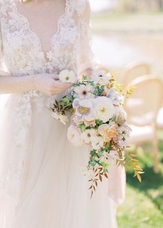 a woman in a wedding dress holding a bouquet of white and peach flowers with greenery