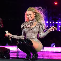 a woman in tights and boots on stage with her legs spread out, smiling at the camera