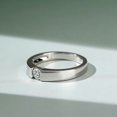 a white gold ring with a single diamond in the center on a plain surface,