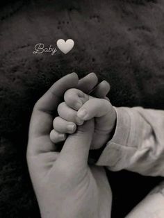 a black and white photo of a baby's hand holding the finger of his mother