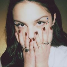 a woman covering her face with both hands and looking at the camera while wearing rings