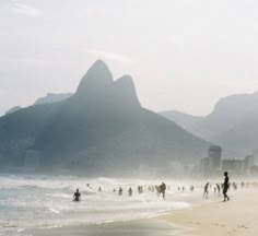 many people are walking on the beach near mountains