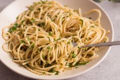 a white bowl filled with pasta and garnished with parsley on the side