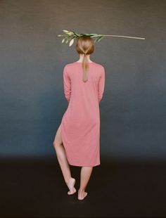 a woman with a flower on her head standing in front of a gray wall wearing a pink dress